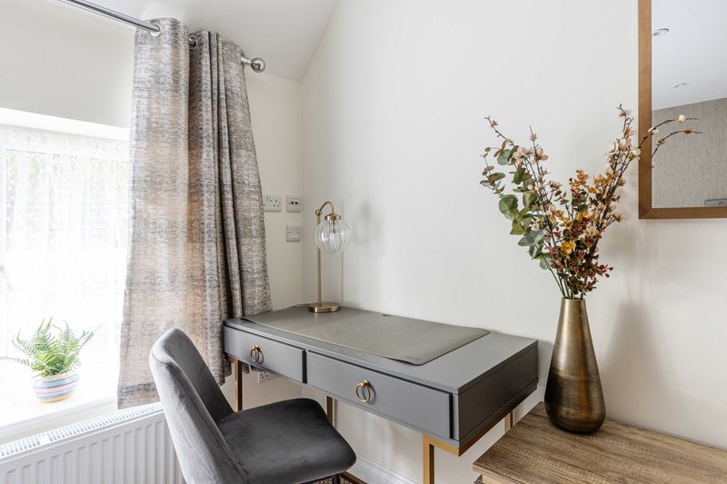 Modern workspace with grey desk, black chair, dried flowers in vase, and window with curtains