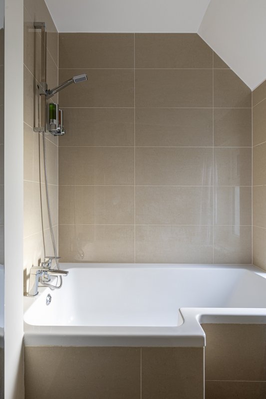 Bathroom with white bathtub, beige tile walls and chrome shower fixtures