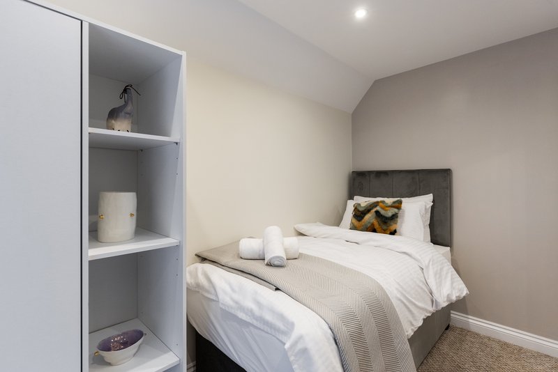 Modern bedroom with double bed, grey headboard, white shelving unit and neutral decor