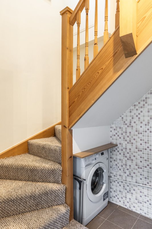 Wooden staircase with carpet runner, washing machine below, tiled wall backdrop