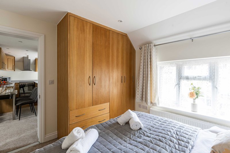 Bright bedroom with wooden wardrobe, double bed, window overlooking garden, and door to ensuite