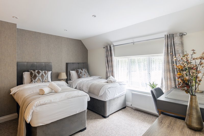 Twin bedroom with two single beds, grey headboards, neutral bedding and window with curtains