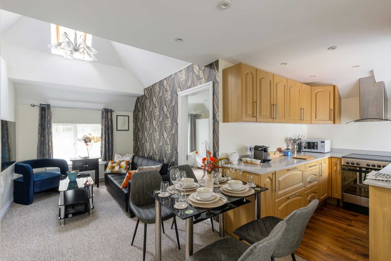 Open-plan kitchen and living area with wooden cabinets, dining table, blue armchair and feature wallpaper