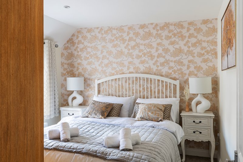 Bedroom with white metal bed frame, patterned wallpaper, wooden nightstands and bedside lamps