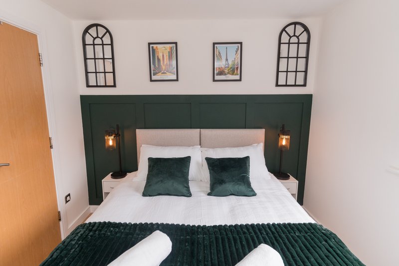 Bedroom with green upholstered headboard, white bedding, dark green pillows and throw blanket