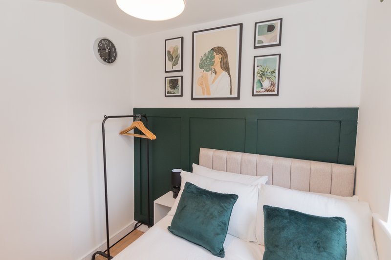 Modern bedroom with green panelled headboard, double bed, teal cushions and framed botanical wall art