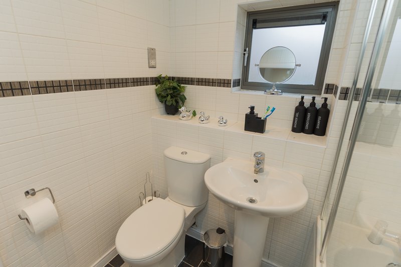 Clean bathroom with white subway tiles, pedestal sink, toilet, window and shower enclosure