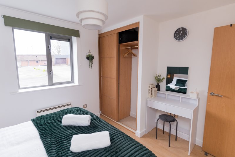 Bedroom with double bed, green bedding, wooden wardrobe, desk, and window with green blind