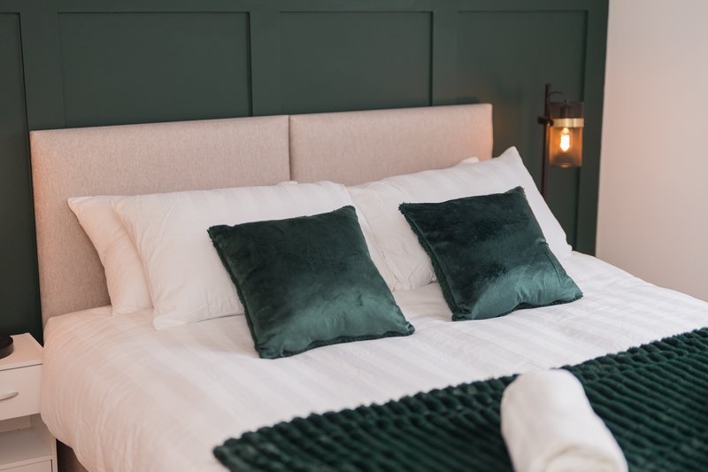 Modern bedroom with upholstered headboard, white bedding, green velvet cushions and throws