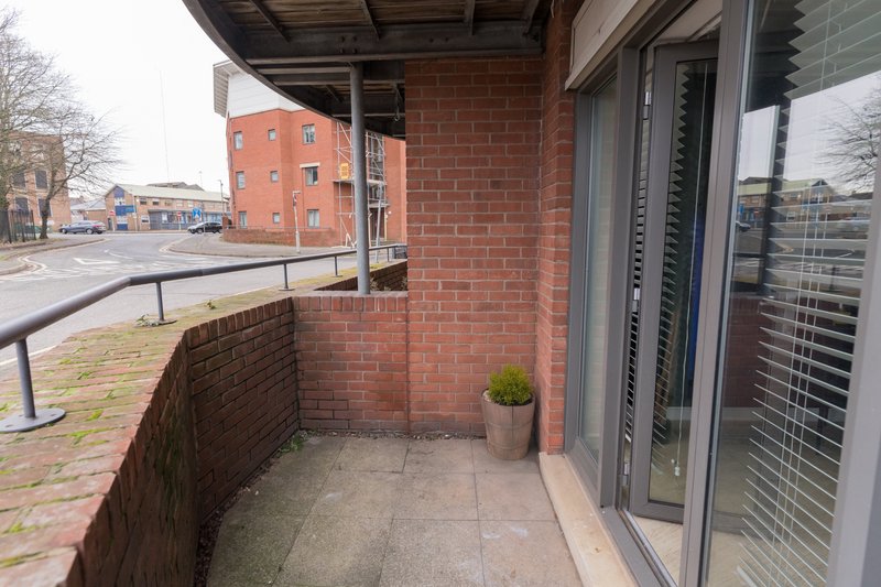 Brick balcony with potted plant, glass doors and urban street view beyond