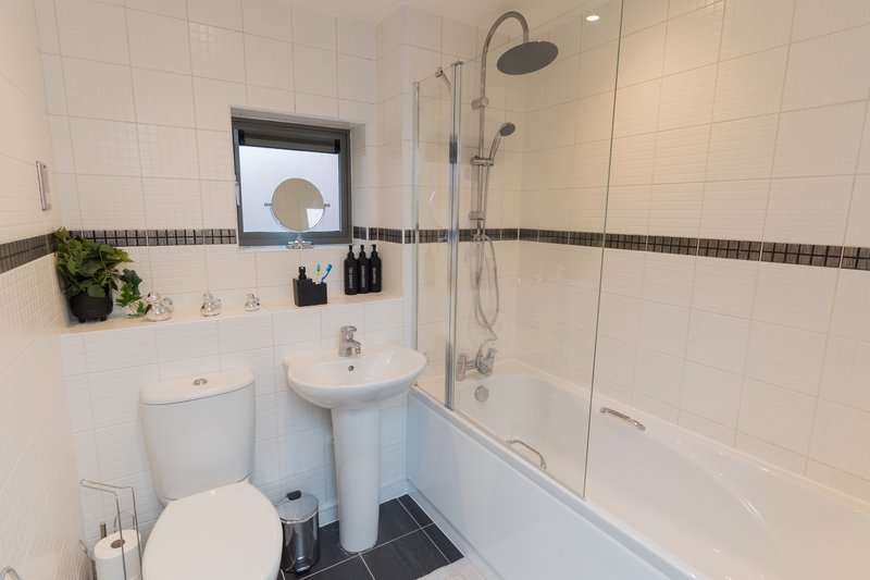 Modern bathroom with white tiles, pedestal sink, toilet, shower bath and window