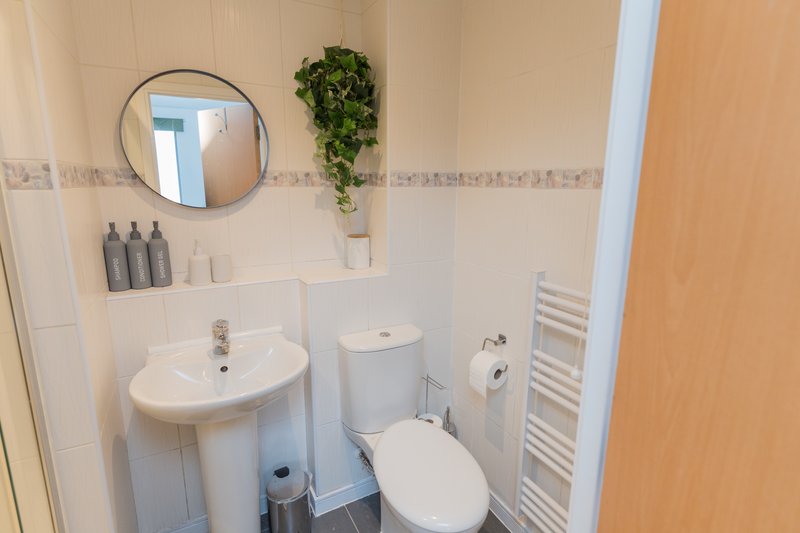 Clean bathroom with white pedestal sink, toilet, round mirror, and towel rail