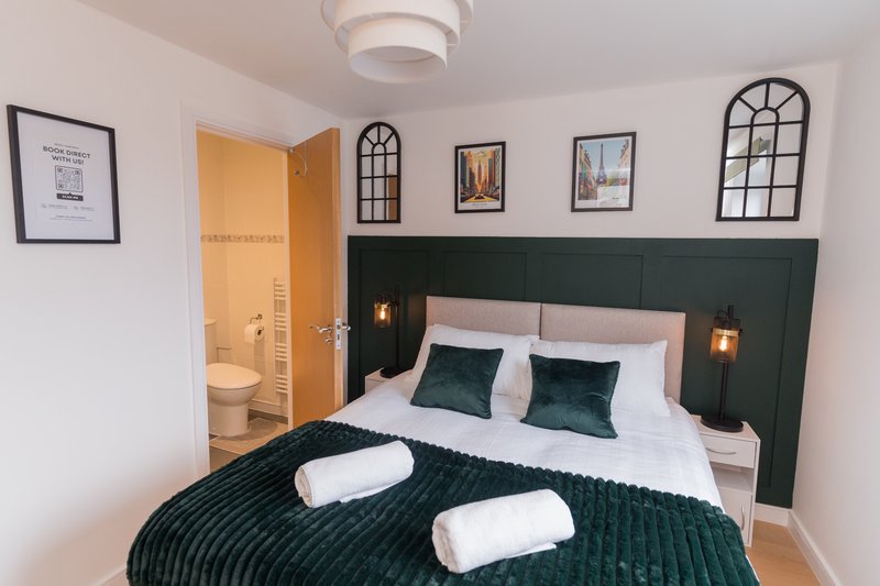 Modern bedroom with double bed, green headboard, white pillows and dark green bedding