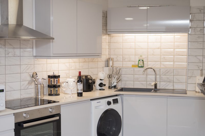 Modern white kitchen with tile backsplash, integrated appliances, and countertop accessories
