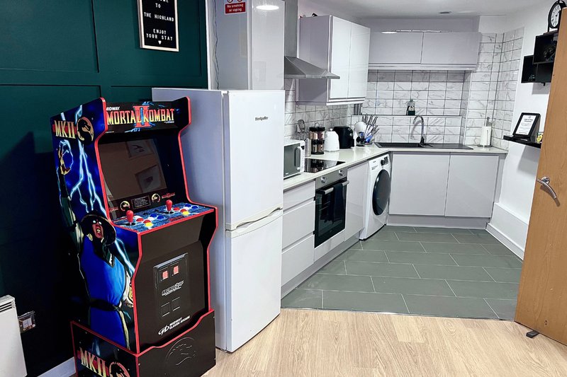 Modern kitchen with white cabinets, gas oven, washing machine, and retro arcade game machine