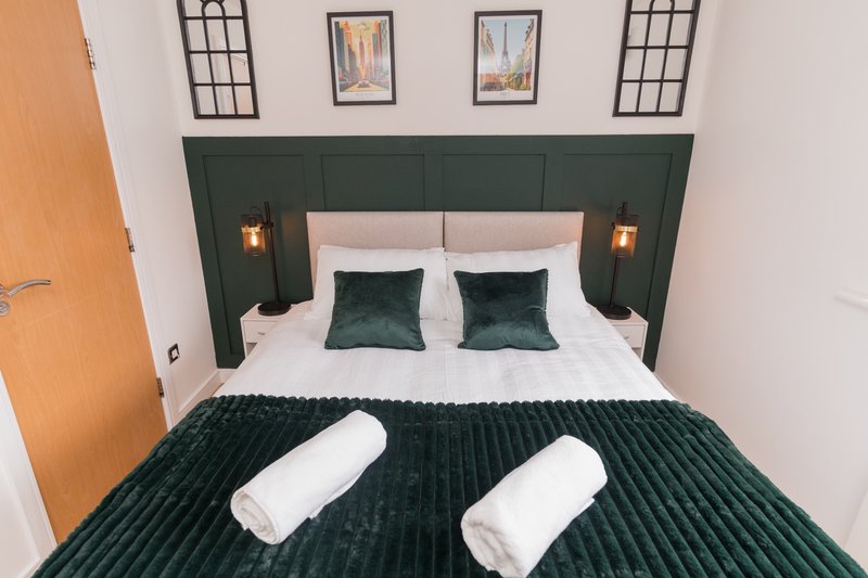 Modern bedroom with green headboard, white bedding, green cushions and rolled towels