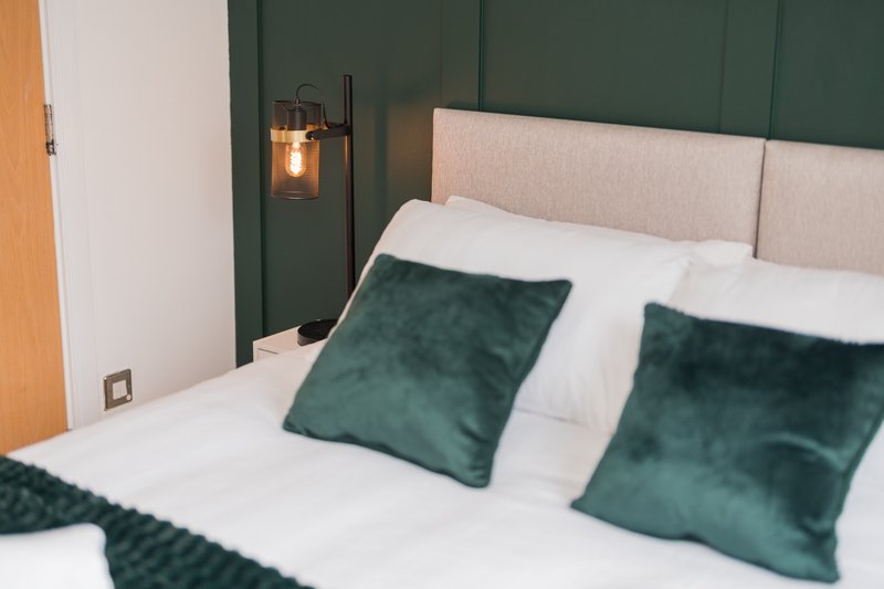 Modern bedroom with double bed, green velvet pillows, beige headboard and pendant light