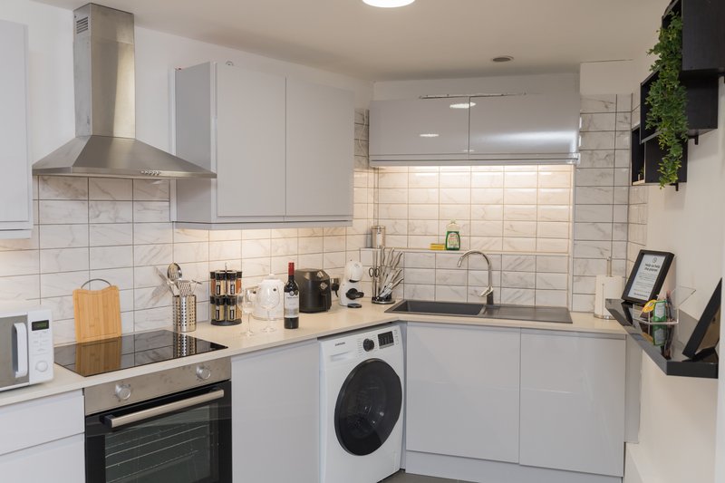 Modern white kitchen with stainless steel appliances, tiled backsplash, and washing machine