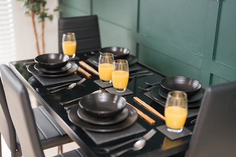 Modern dining table set with black plates, cutlery, and orange juice glasses