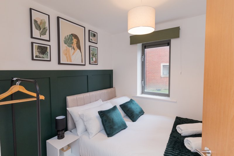 Compact bedroom with green headboard, white bedding, teal cushions and framed botanical artwork