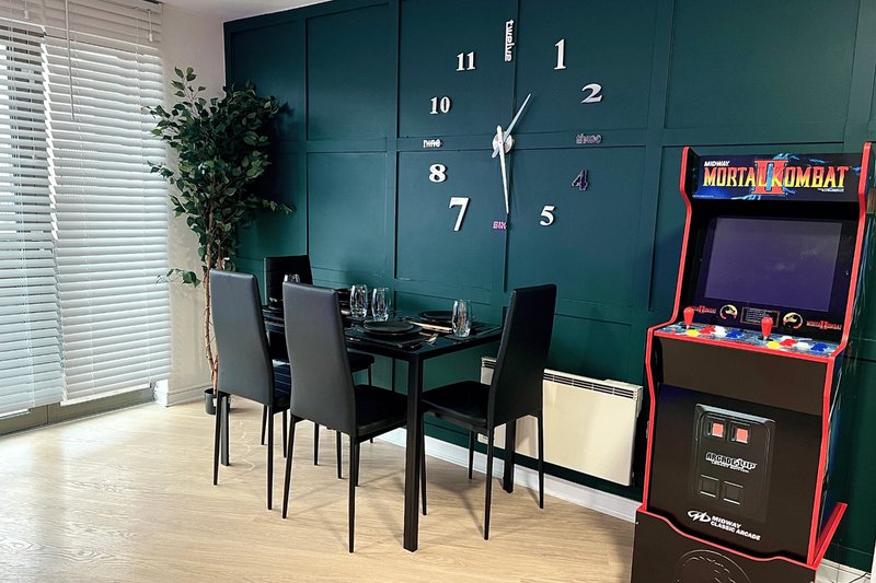 Modern dining area with black table, chairs, wall clock, and arcade game cabinet