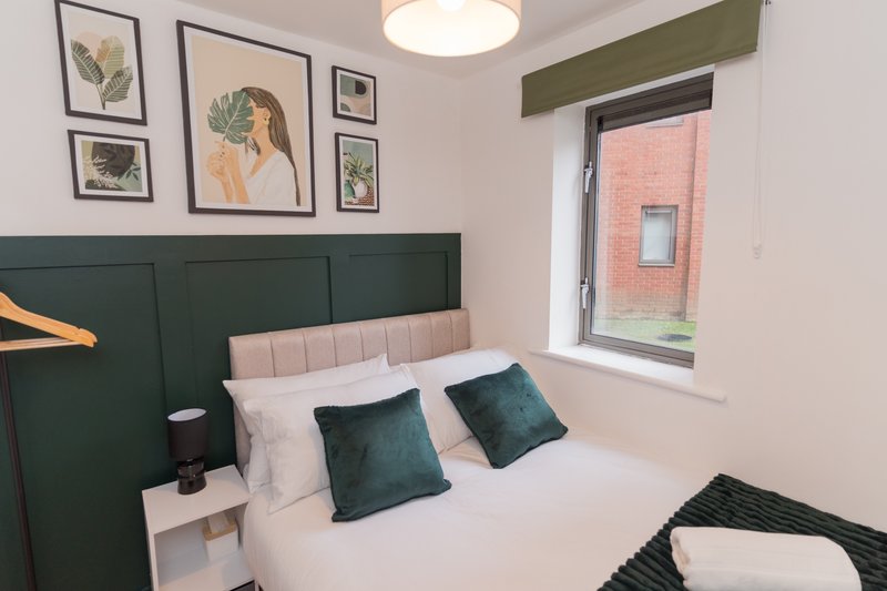Modern bedroom with green headboard, white bedding, decorative cushions and framed wall art