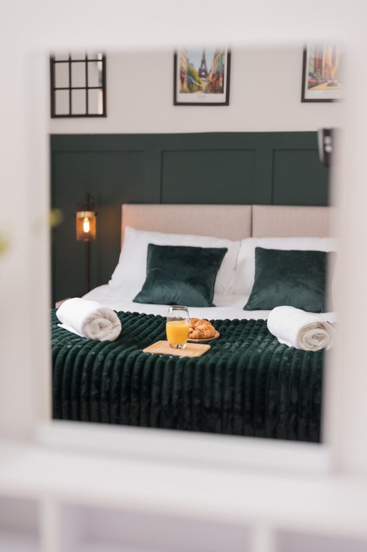Bedroom with dark green upholstered headboard, white pillows, green cushions and black bedding
