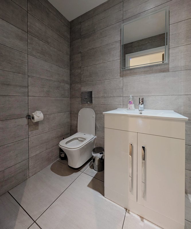 Modern bathroom with toilet, cream vanity unit, sink, and grey tile walls