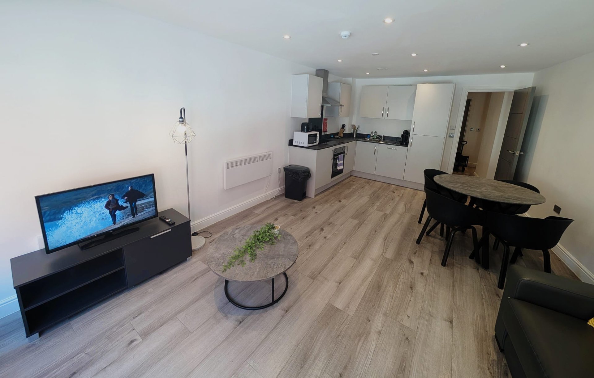 Open-plan living room with TV, dining table, kitchen area and wooden flooring