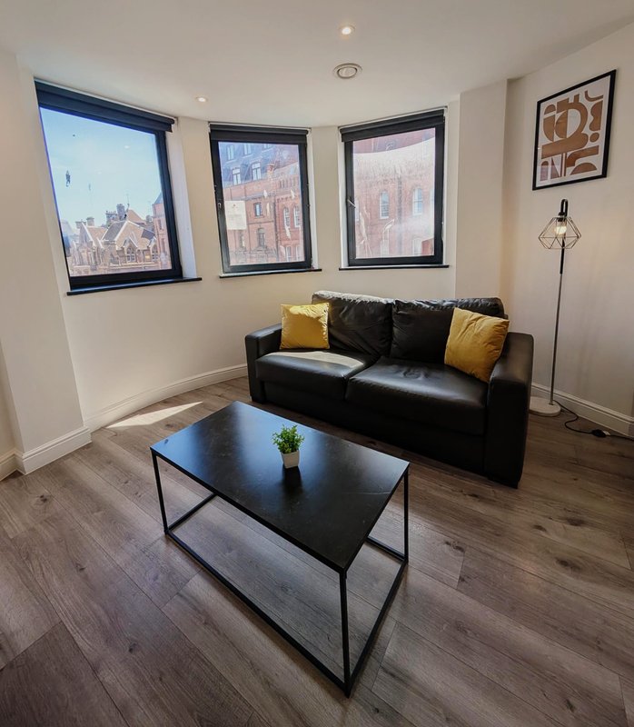 Modern living room with black leather sofa, yellow cushions, black coffee table, and city views through three windows