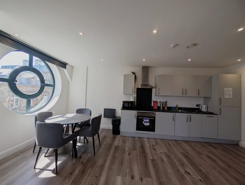 Modern open-plan kitchen and dining area with grey cabinetry, black dining table and chairs, and circular wall art