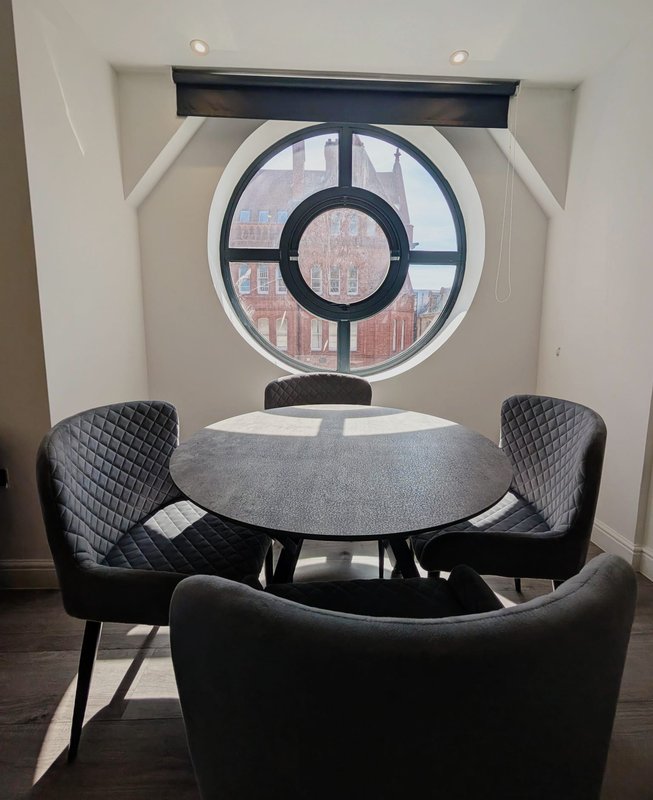 Modern dining area with round table, black chairs, and circular window overlooking city