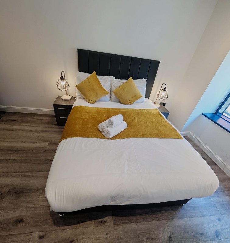 Modern bedroom with black upholstered bed, yellow cushions, white pillows and bedside lamps