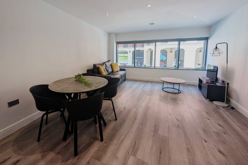 Open-plan living and dining area with wooden flooring, round table, black chairs, and sofa by large windows