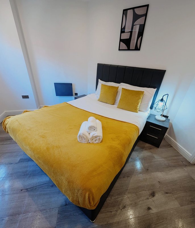 Bedroom with double bed, yellow bedding, black headboard, wooden floor and wall art