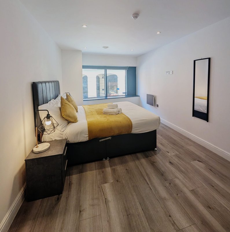 Modern bedroom with double bed, yellow bedding, wooden floor and city view windows