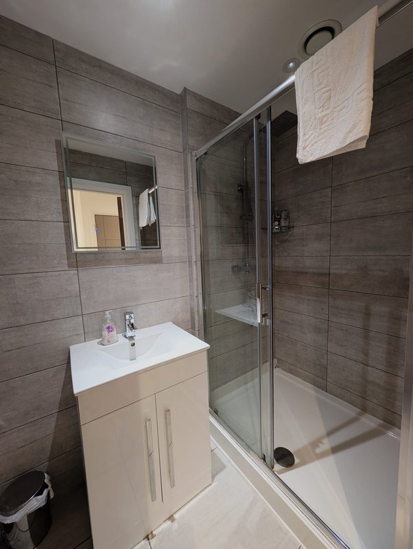 Modern bathroom with grey tile walls, white vanity, mirror, and shower enclosure