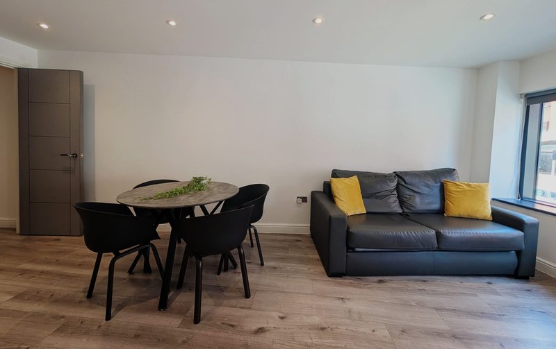Modern open-plan living space with dining table, black chairs, and navy leather sofa with yellow cushions