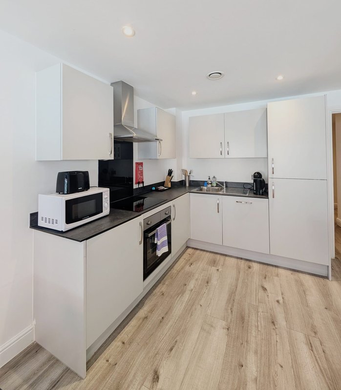 Modern white kitchen with black countertops, integrated appliances, and wooden flooring