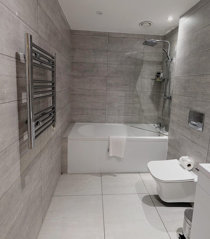 Modern bathroom with walk-in shower, white bathtub, toilet, heated towel rail and grey tile walls