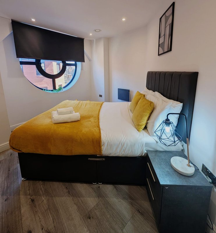 Modern bedroom with double bed, yellow bedding, wall-mounted TV, and black headboard