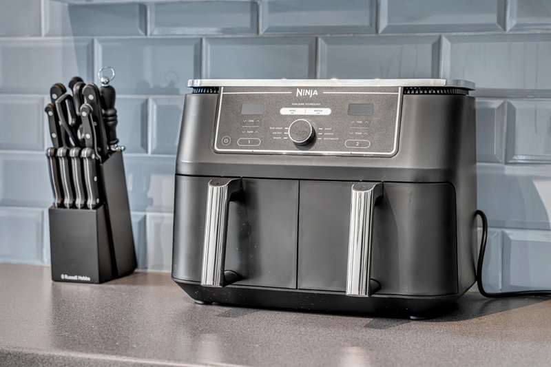 Kitchen countertop with Ninja air fryer and knife block set against subway tile backsplash