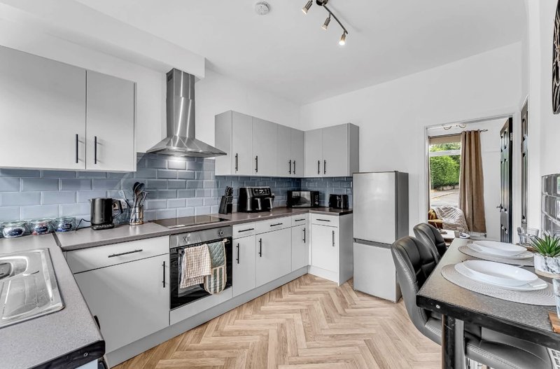 Modern kitchen with white cabinetry, gray subway tiles, stainless steel appliances and herringbone wooden flooring