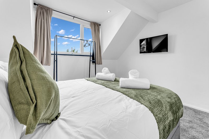 Bright attic bedroom with double bed, green throw blanket, white bedding and large window