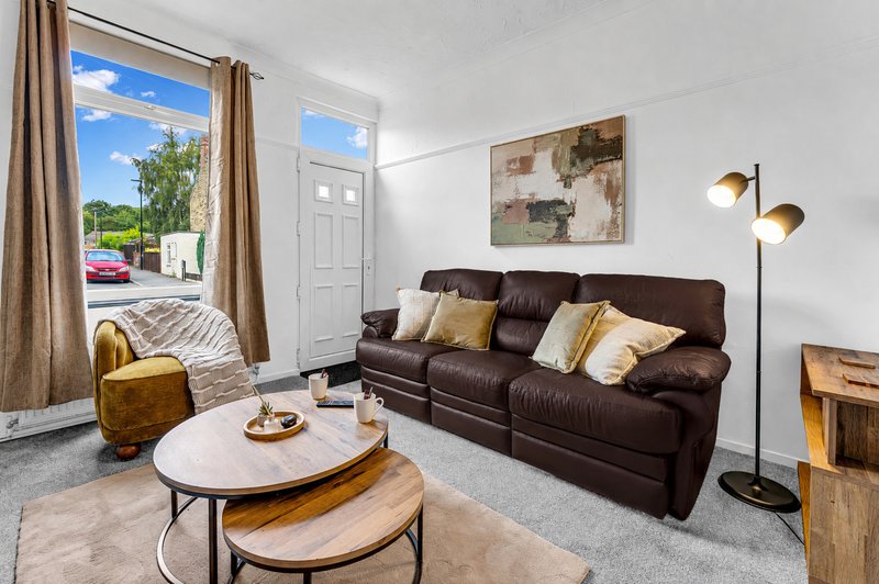 Bright living room with brown leather sofa, wooden coffee table, gold accents and large windows overlooking driveway