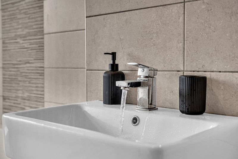 Modern bathroom sink with chrome faucet, soap dispenser, and ceramic accessories