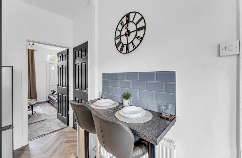 Modern kitchen with dining table, two chairs, blue tile backsplash and wall clock