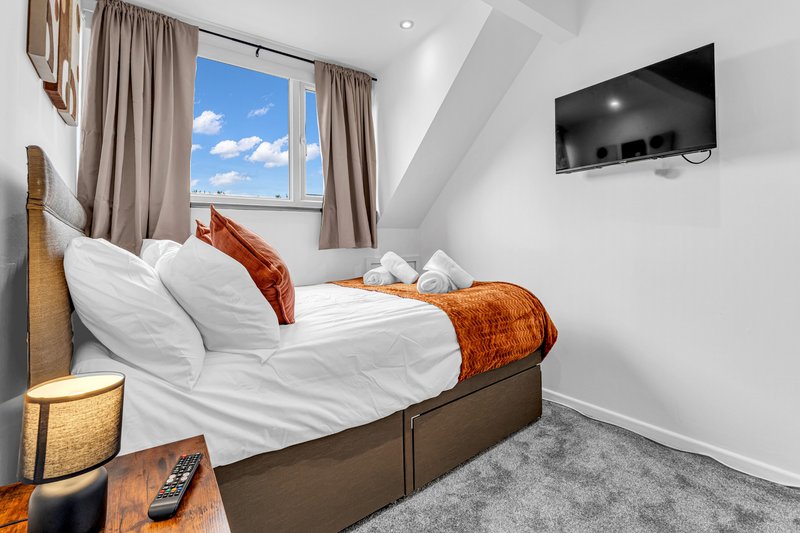 Modern bedroom with double bed, white bedding, orange throws, wall-mounted TV and large window