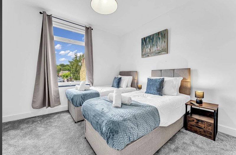 Bright bedroom with two single beds, blue bedding, window with countryside view, and wooden nightstand.