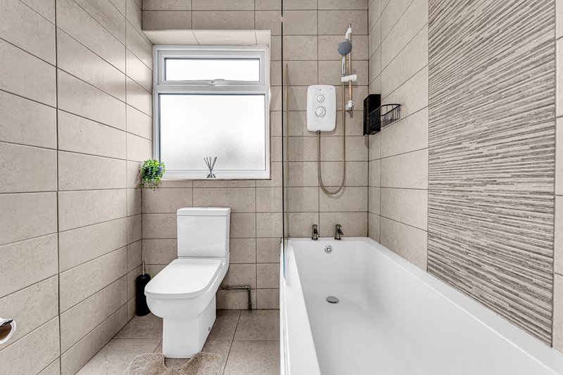 Modern bathroom with toilet, bathtub, tiled walls, window and shower fixtures